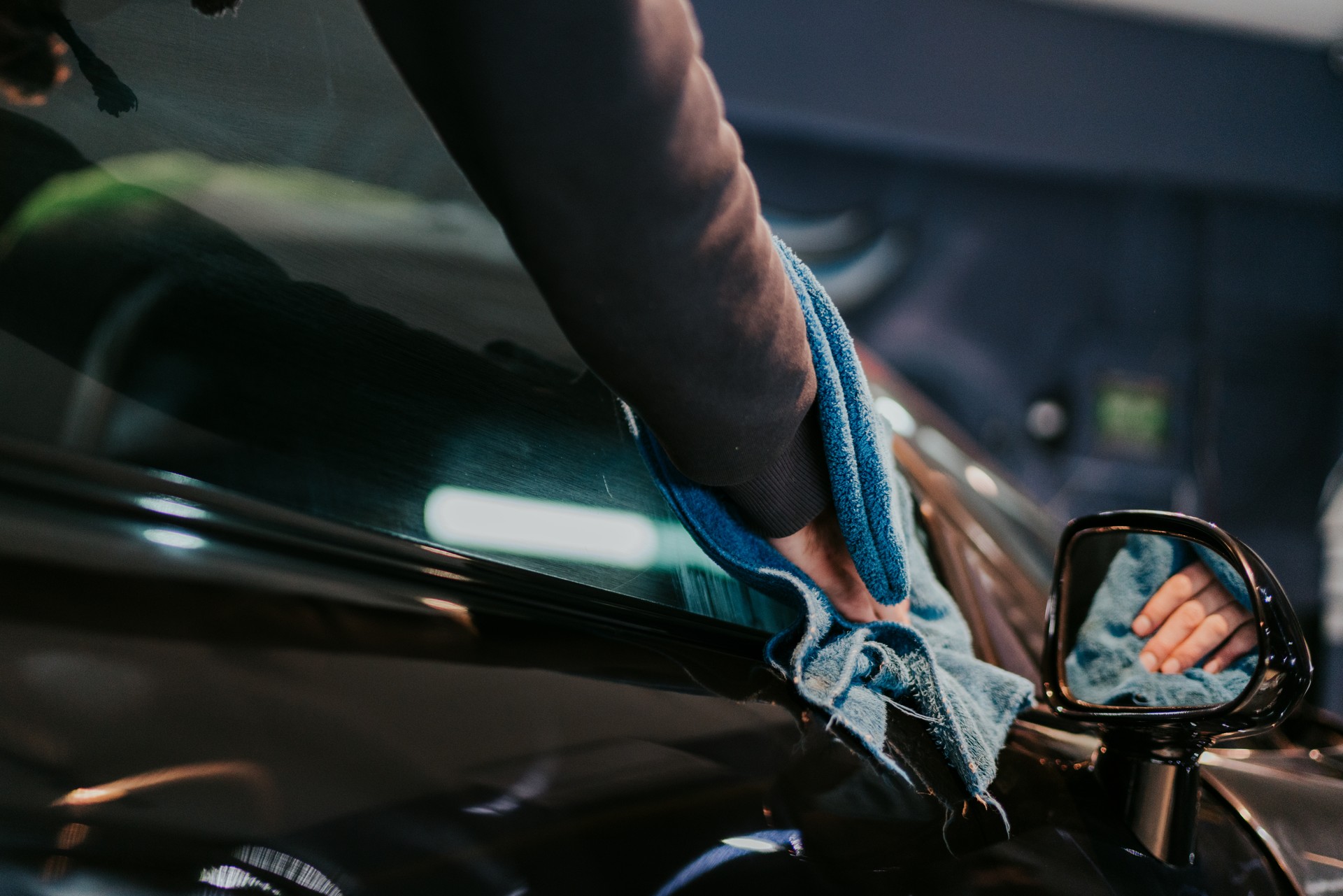 A man cleaning a car with blue microfiber cloth - car detailing, vale and auto service concept